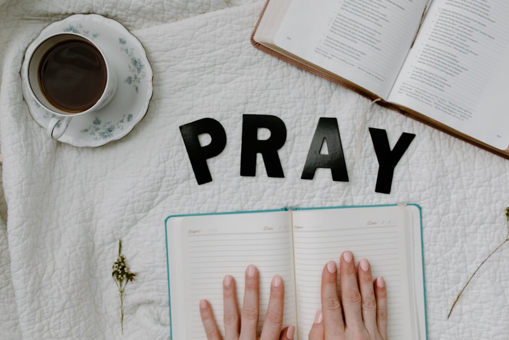 A serene flat lay featuring an open Bible, a journal, and a cup of coffee with the word 'PRAY'.