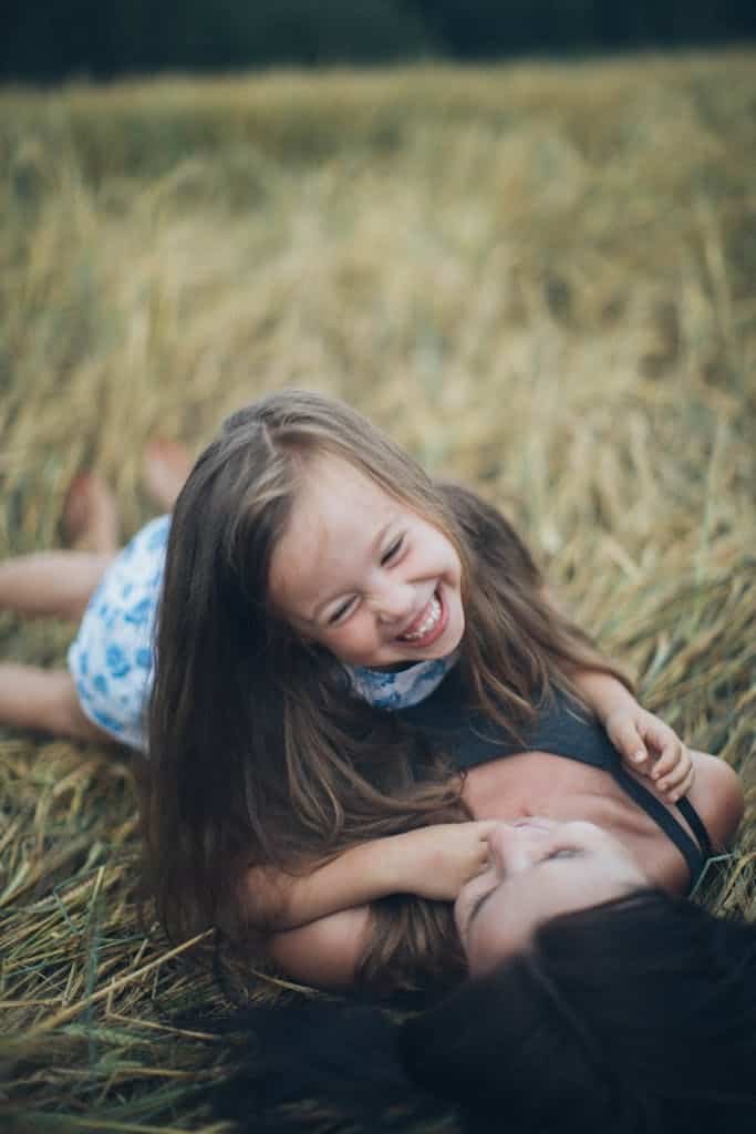 A joyful mother and daughter sharing a playful moment in a sunlit summer field.