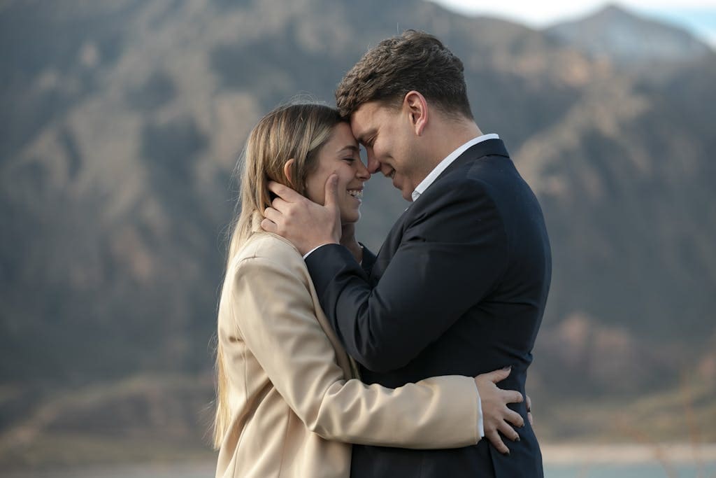 A loving couple embraces with mountains in the background, showcasing romance and connection.