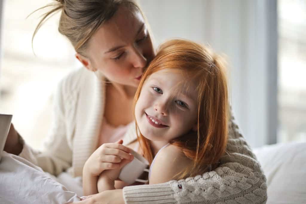 A mother tenderly hugging her smiling daughter indoors, showcasing love and warmth.