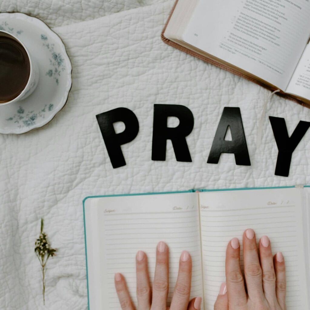 A serene flat lay featuring an open Bible, a journal, and a cup of coffee with the word 'PRAY'.