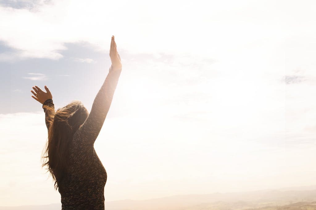 A woman with raised arms enjoying the bright open sky in a serene outdoor setting.