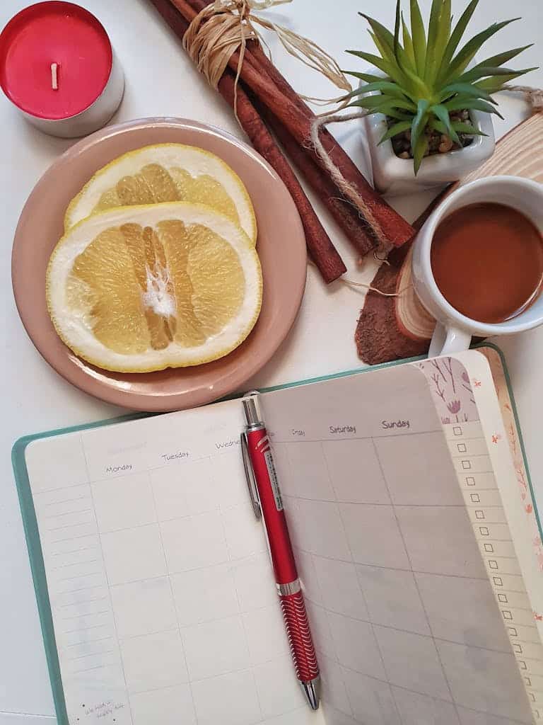 Flat lay of morning essentials including coffee, grapefruit, planner, and candle on a white table.