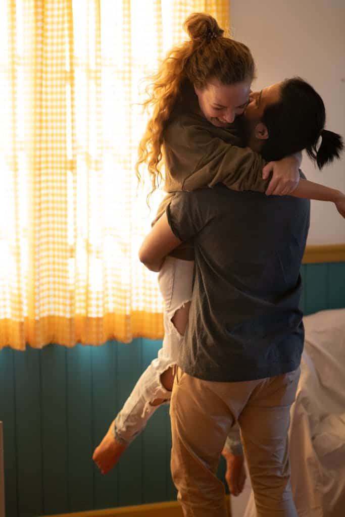 Joyful moment of a couple hugging in their cozy, sunlit living room.