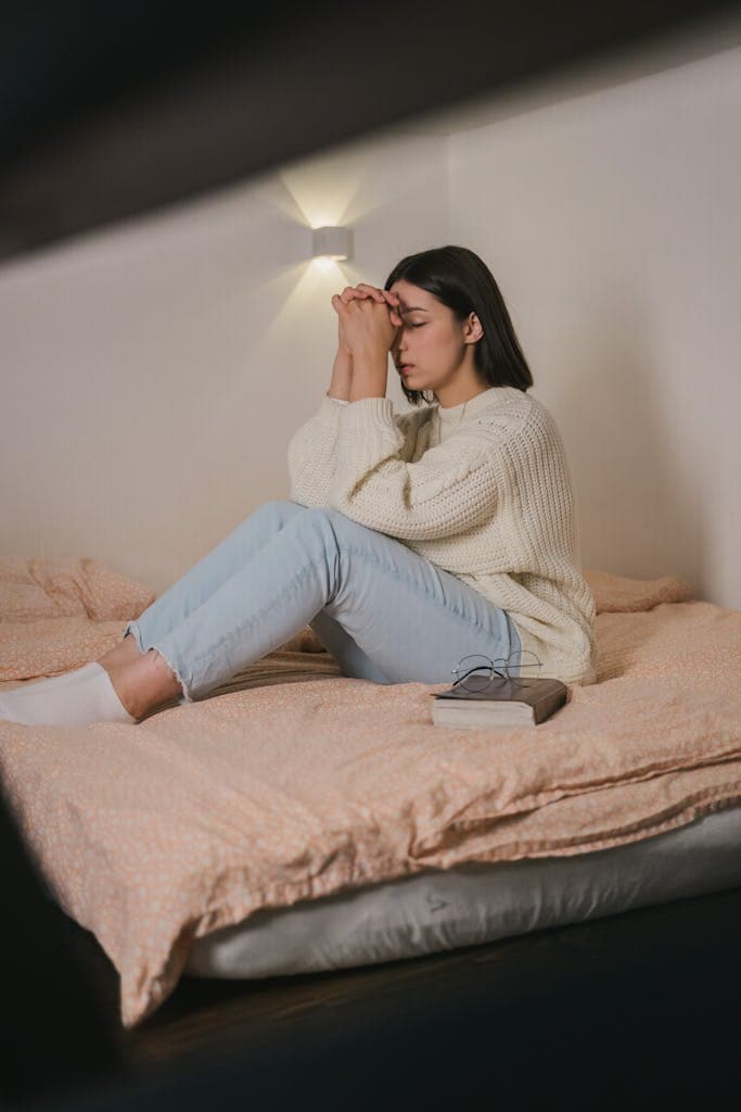 Woman in a cozy bedroom, wearing comfort clothes, meditating with eyes closed.