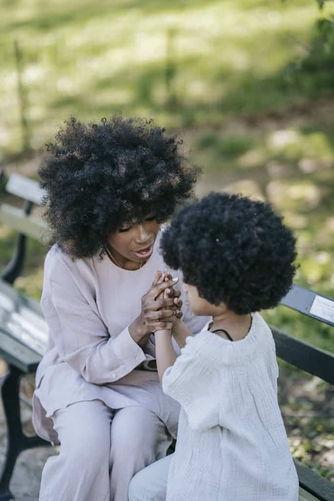 A loving moment between a mother and daughter sitting on a park bench enjoying quality time.