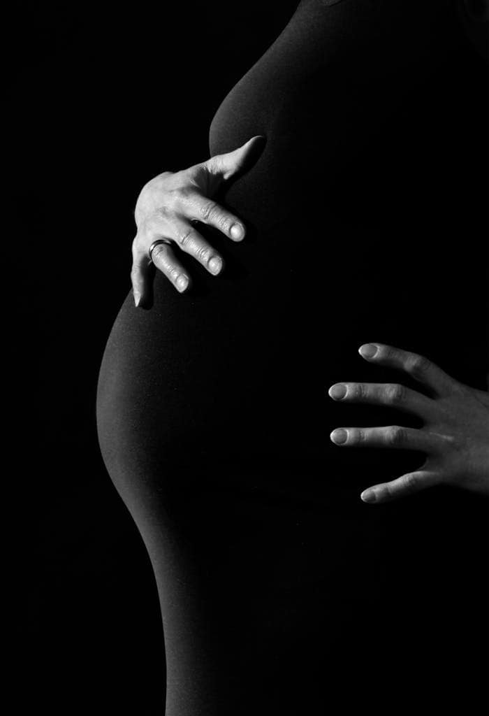 Artistic black and white portrait of pregnant woman embracing belly.