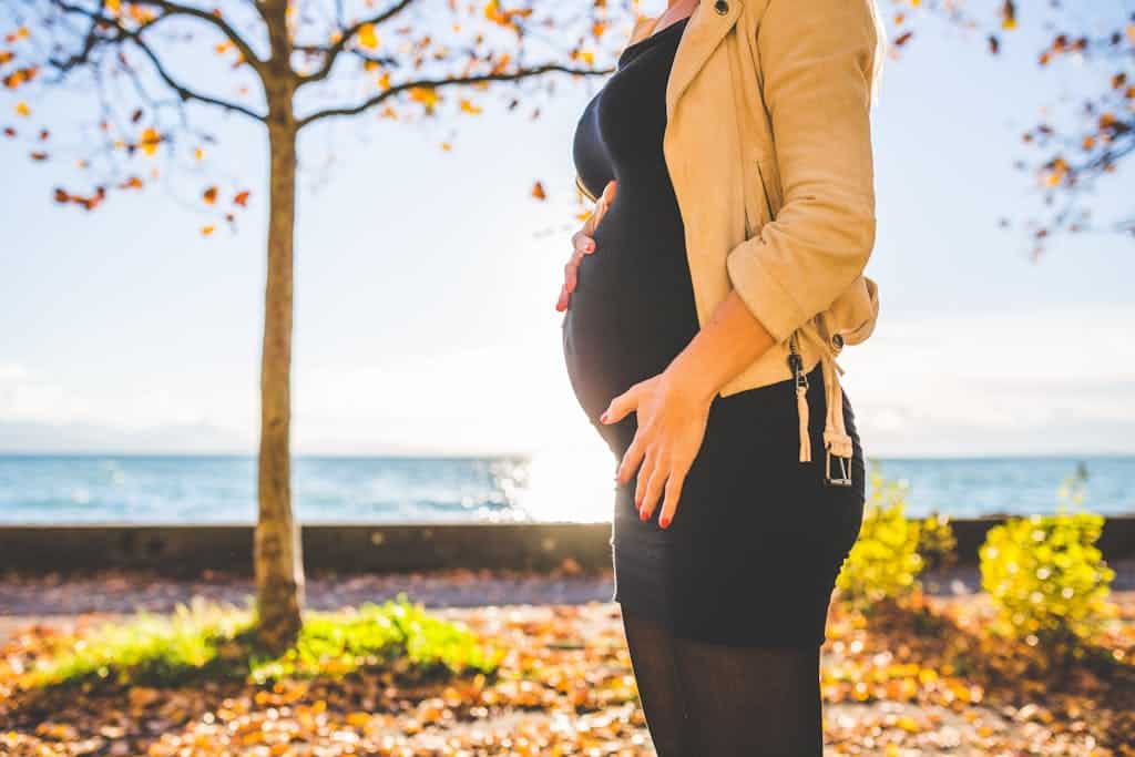 Expectant mother embracing nature during a fall day by the ocean.